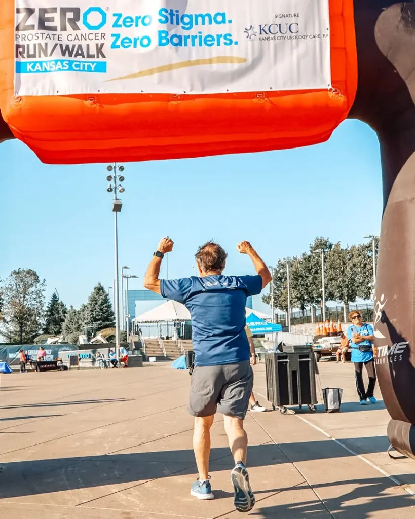 A 2025 ZERO Prostate Cancer Run/Walk participant crossing the finish line, arms raised.